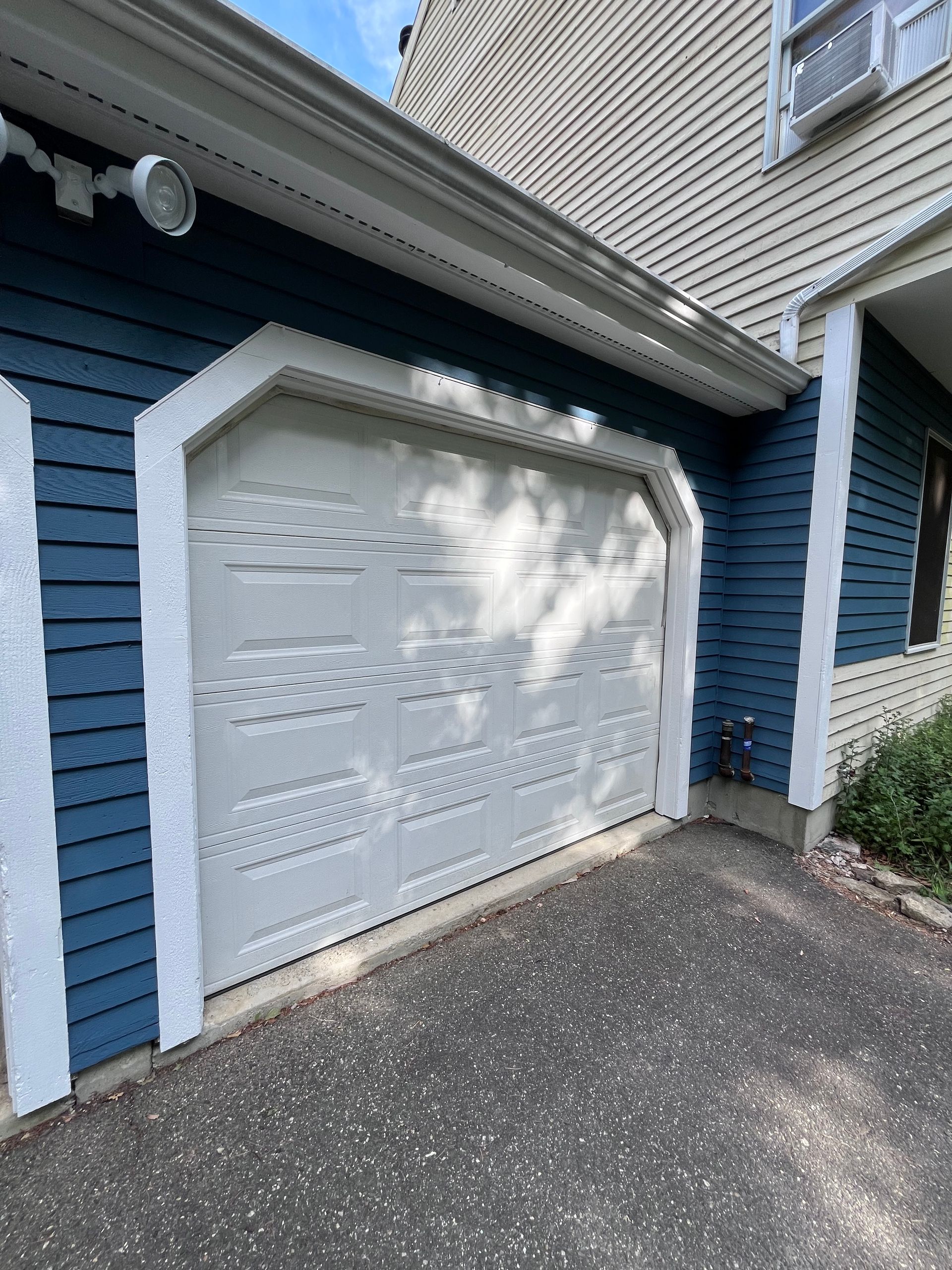 A white garage door is sitting in front of a blue house.