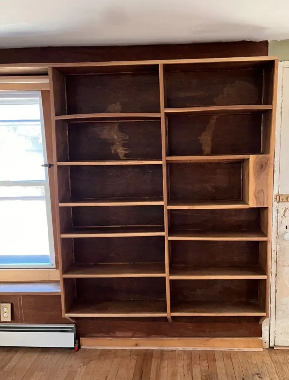 An empty bookshelf in a living room next to a window.
