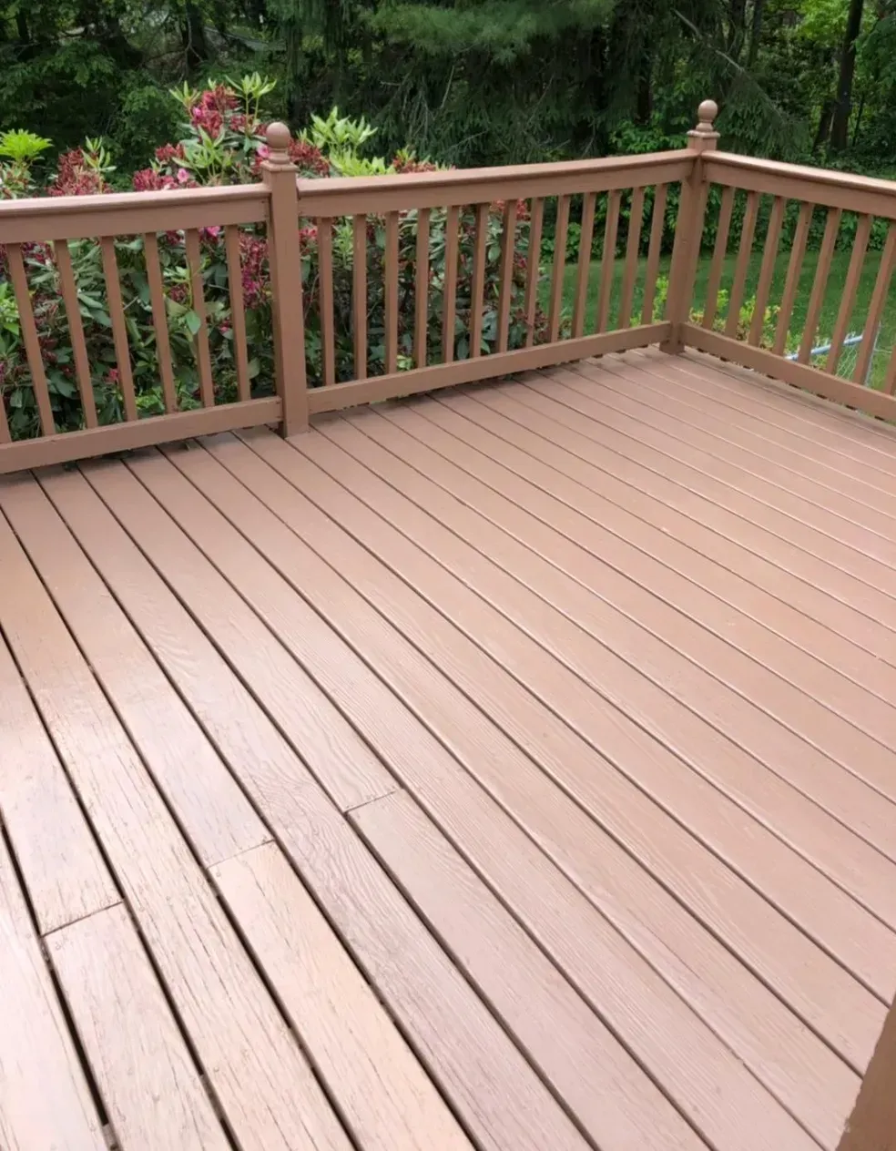 A wooden deck with a railing and flowers in the background.