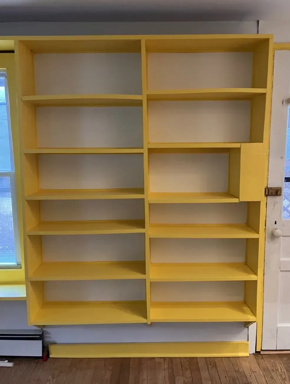A large yellow bookshelf is in a room next to a door.