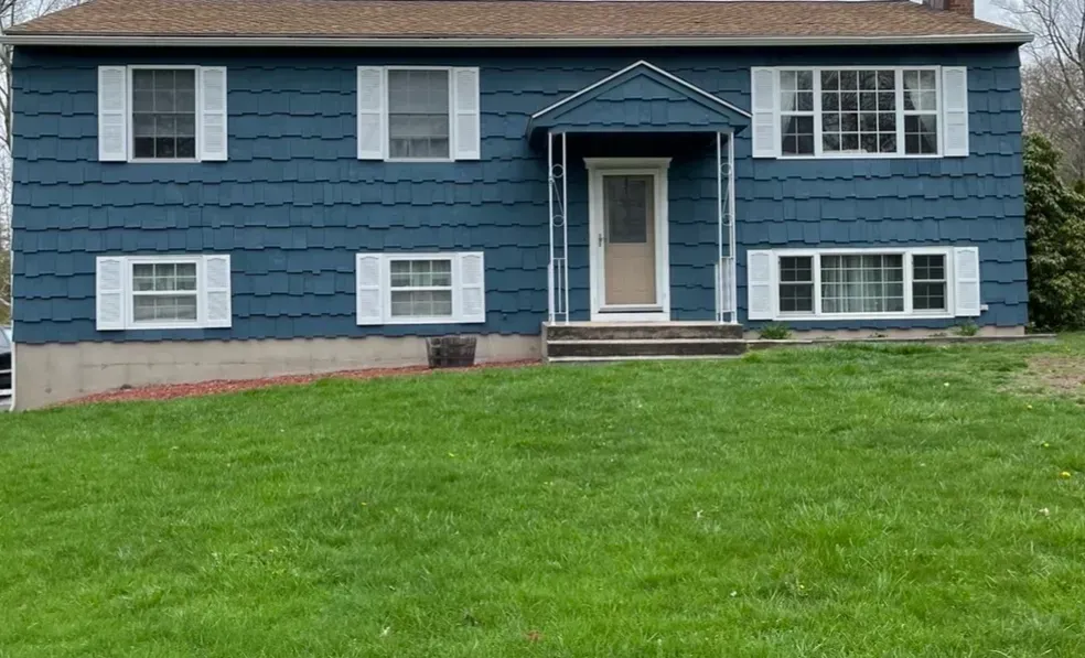 A blue house with white shutters and a large lawn in front of it.
