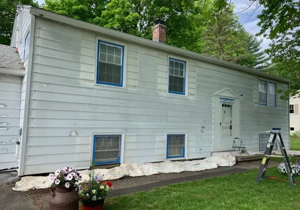 A white house with blue trim is being painted.