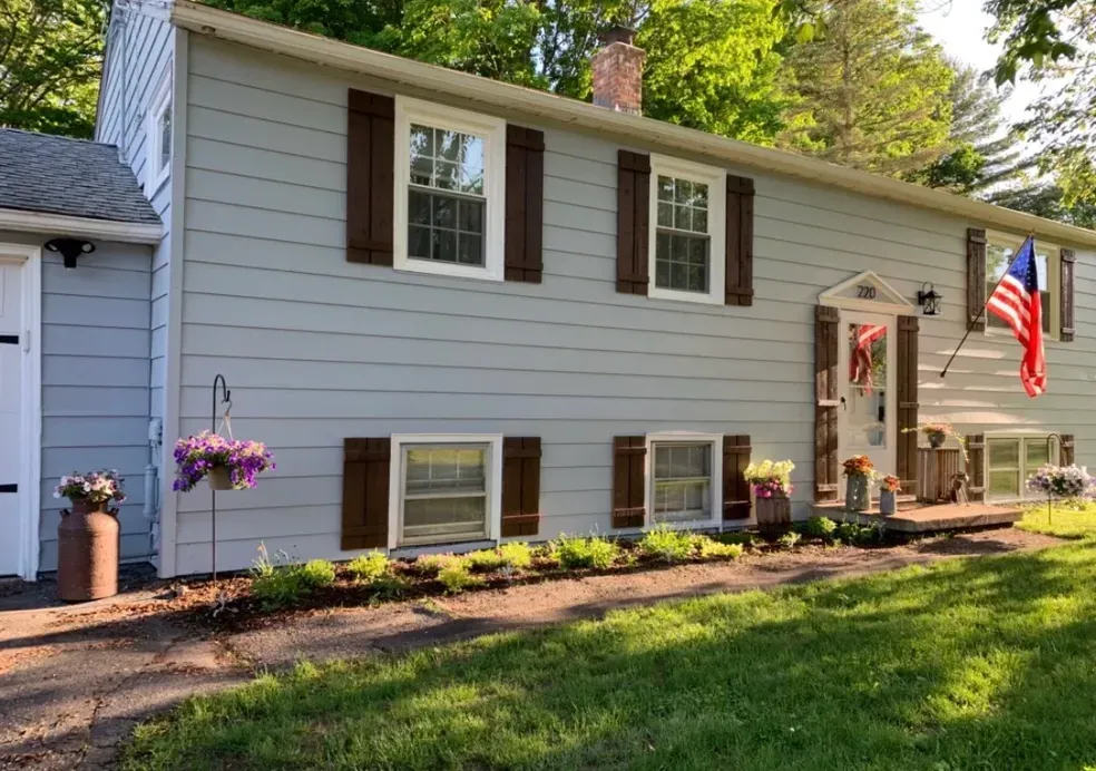 The front of a house with brown shutters and a flag on the porch.