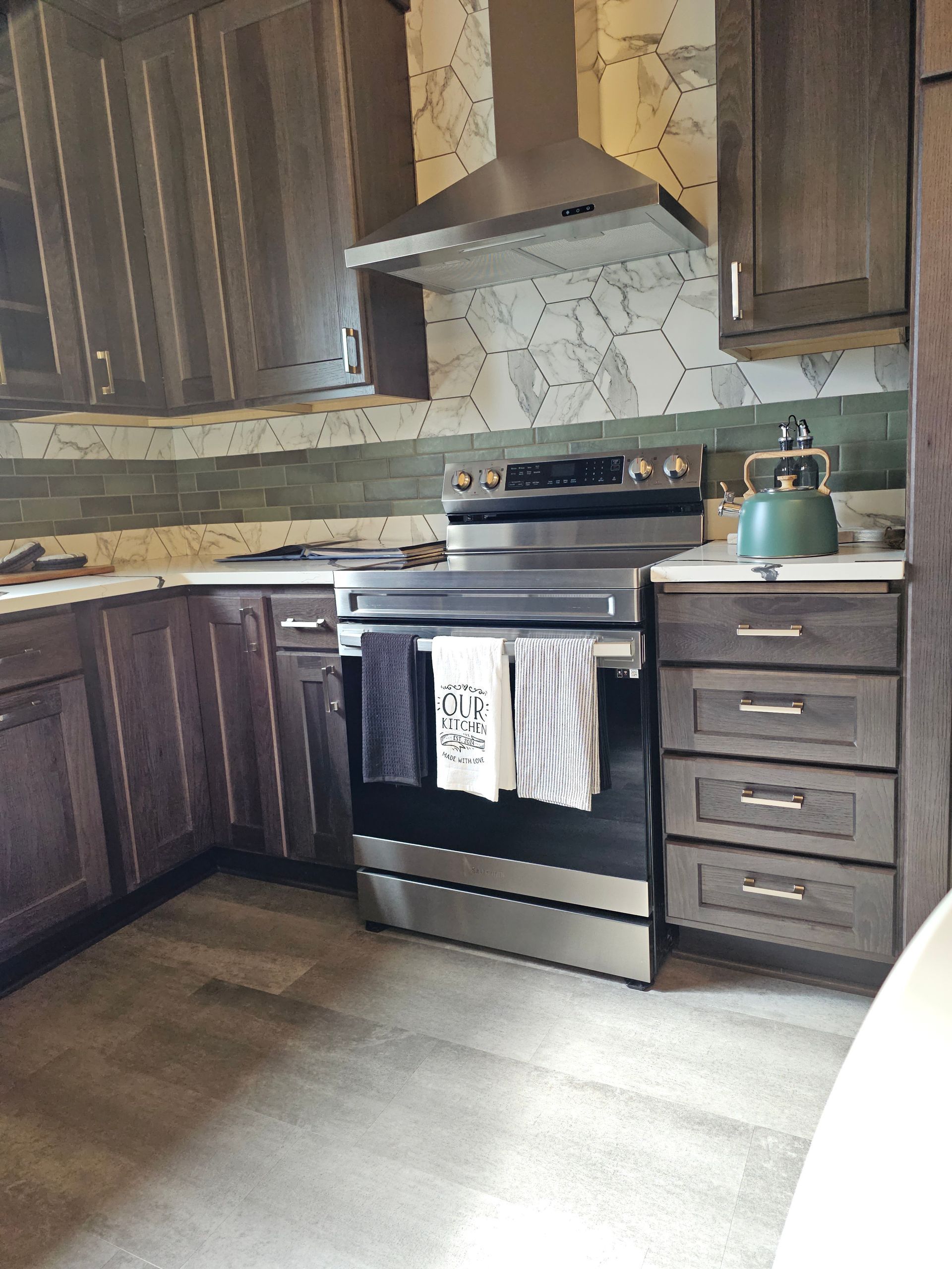 Kitchen with stainless steel stove, cabinets, and patterned backsplash. Gray and white towels hang on the oven.