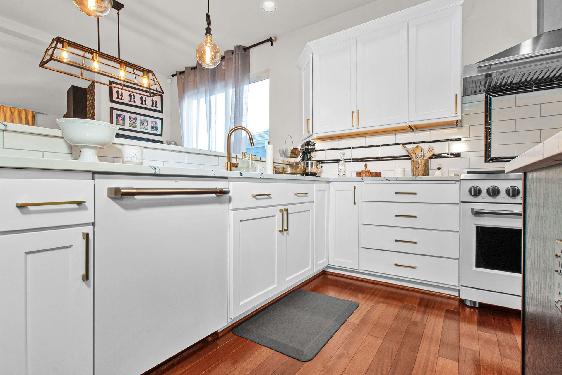 A kitchen with white cabinets , hardwood floors , stainless steel appliances and a rug on the floor.