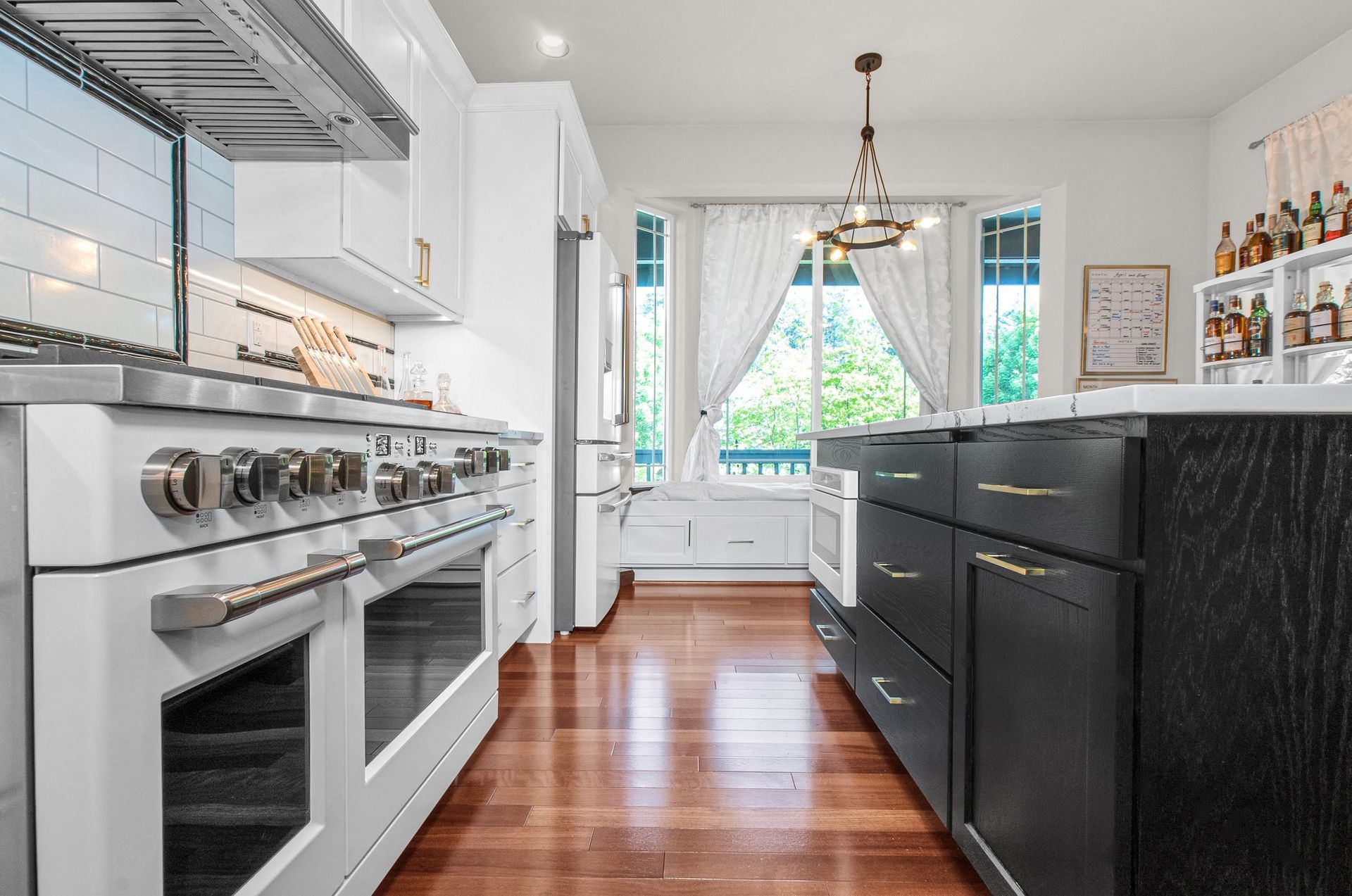 A kitchen with white appliances , black cabinets and hardwood floors.