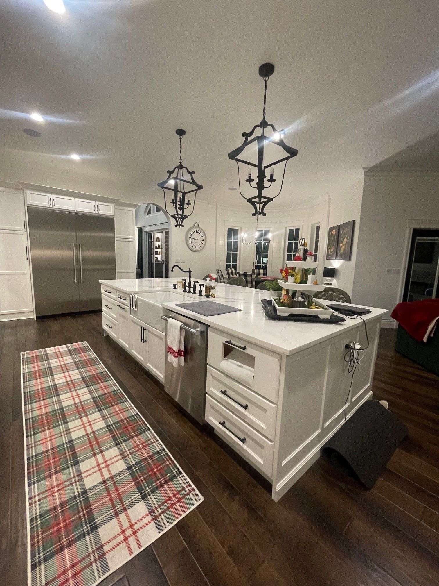 A kitchen with white cabinets , hardwood floors , stainless steel appliances and a rug on the floor.