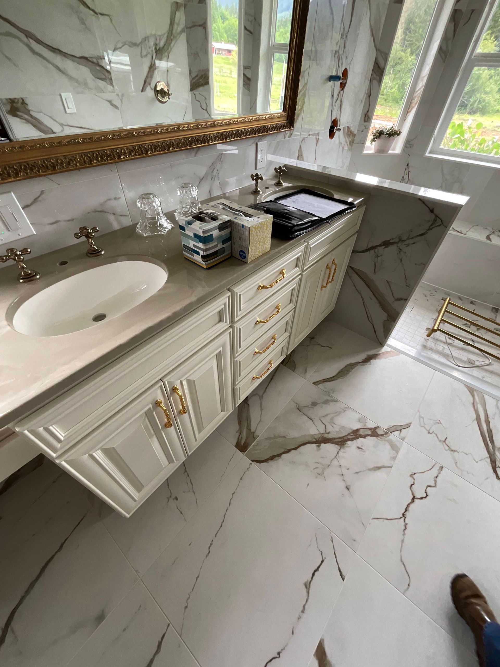 Luxury bathroom with marble floor and countertop, white cabinets, gold accents, and large mirror.