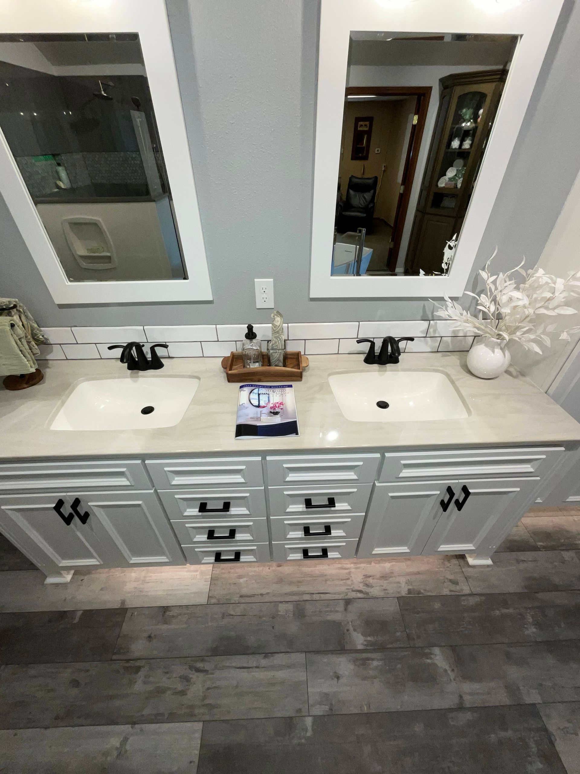 Bathroom vanity with two sinks, two mirrors, and white cabinets. Gray walls and wood-look flooring.