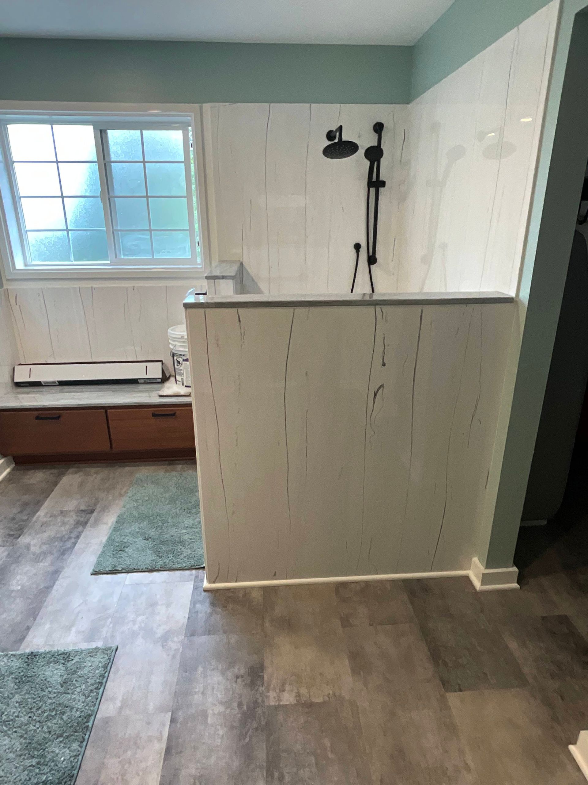Bathroom with a shower, window, and wood-look flooring. Light-colored wall panels and a black showerhead.