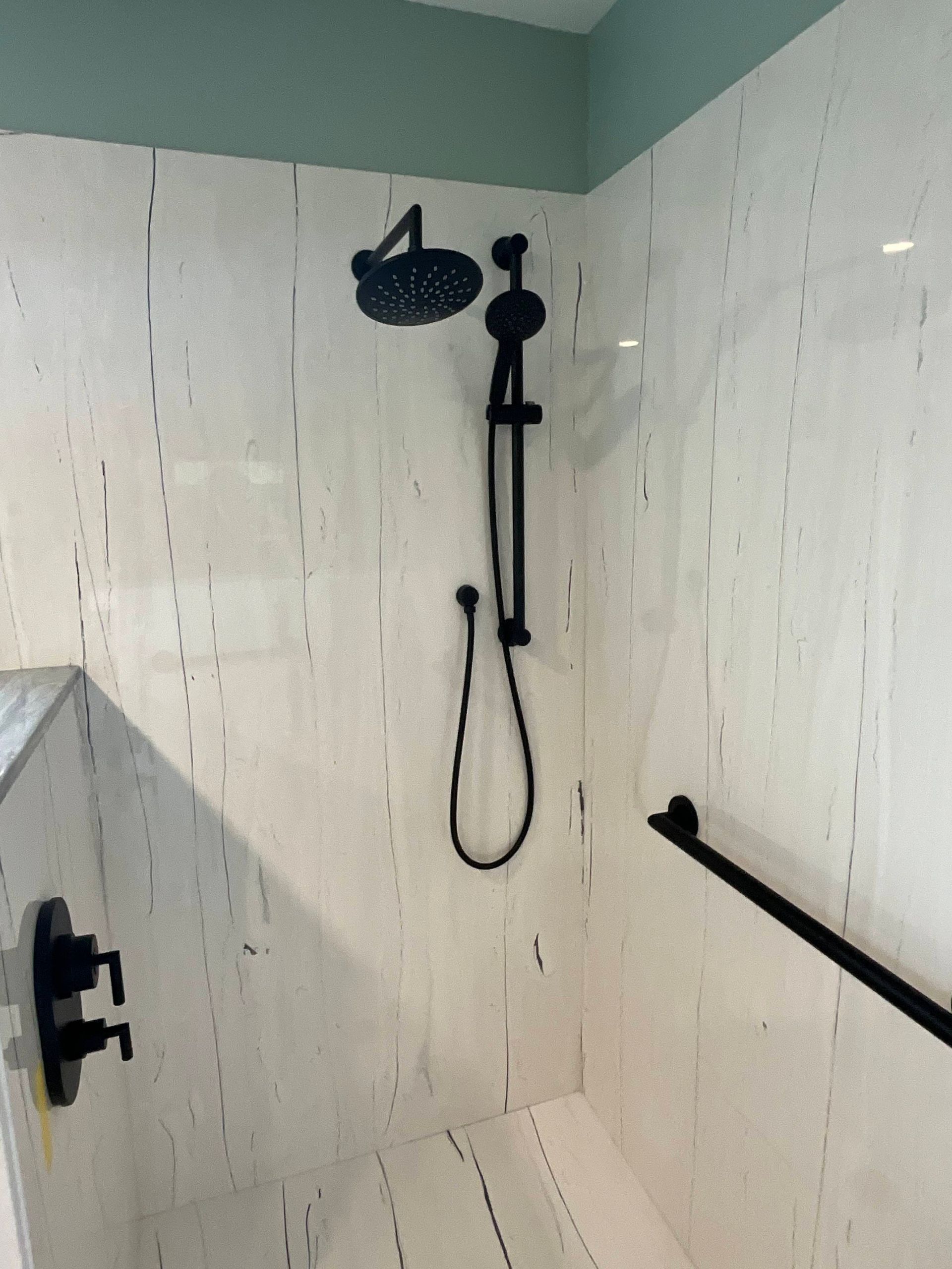 Black shower fixtures on white tiled wall with grab bar.