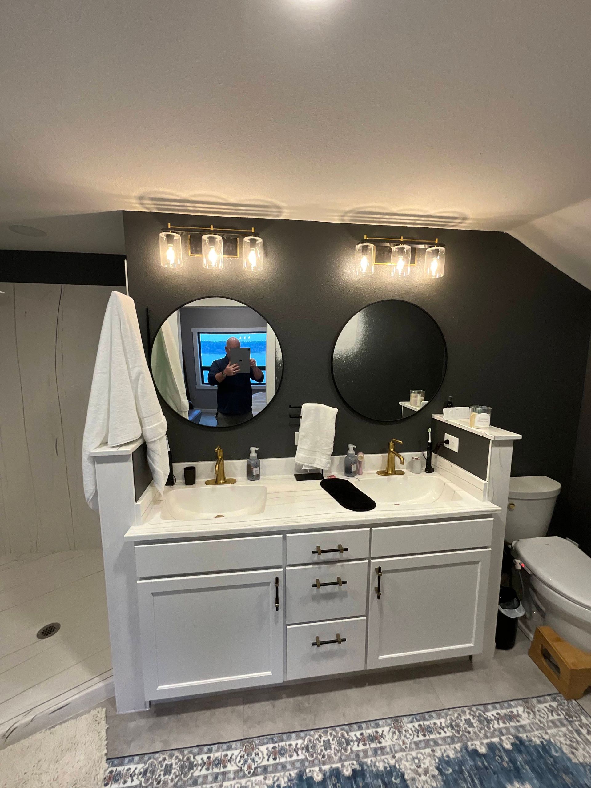 Bathroom with white double vanity, round mirrors, dark gray wall, and overhead lights.