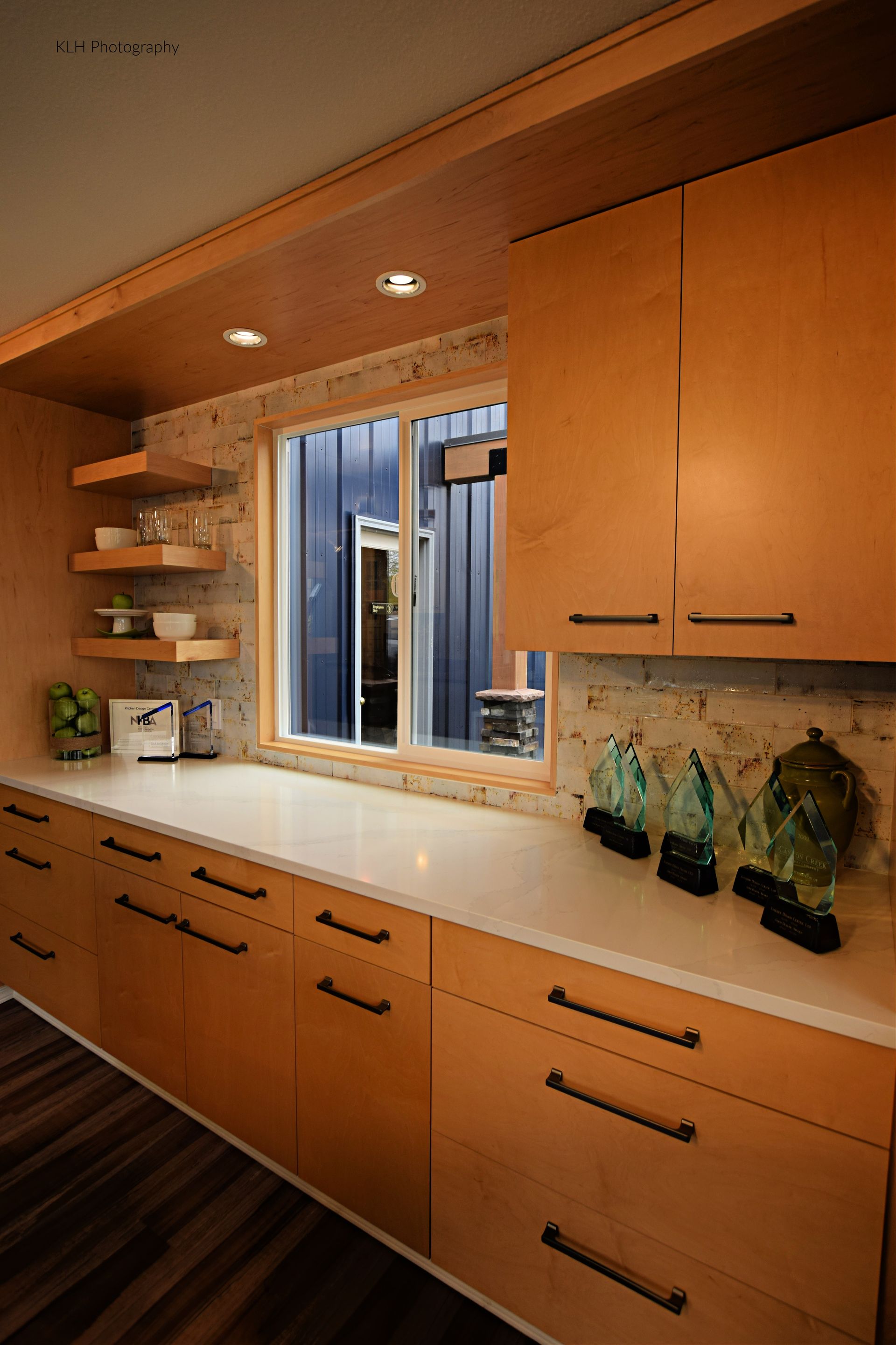 A kitchen with wooden cabinets , white counter tops , and a window.