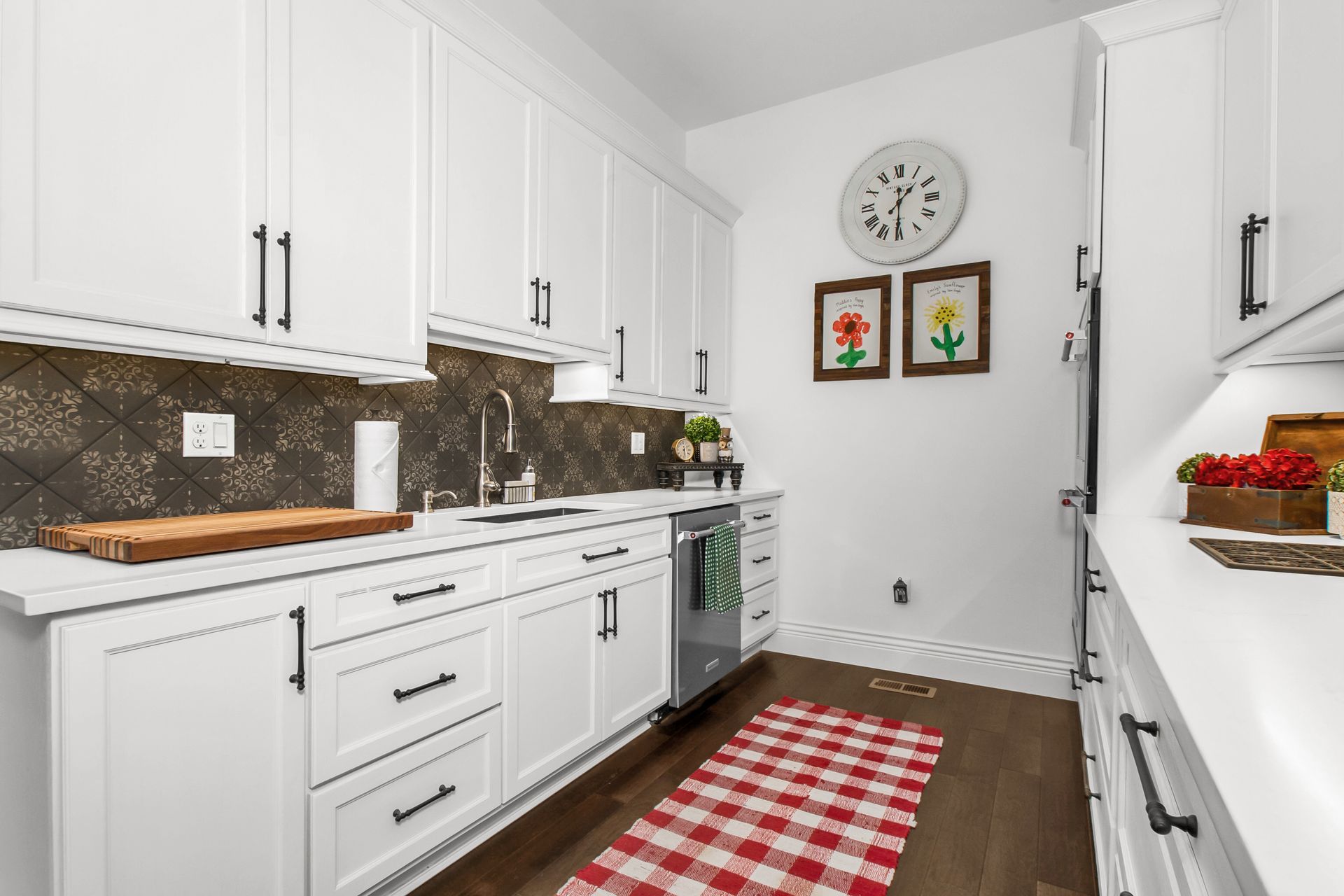 A kitchen with white cabinets and a red and white checkered rug.