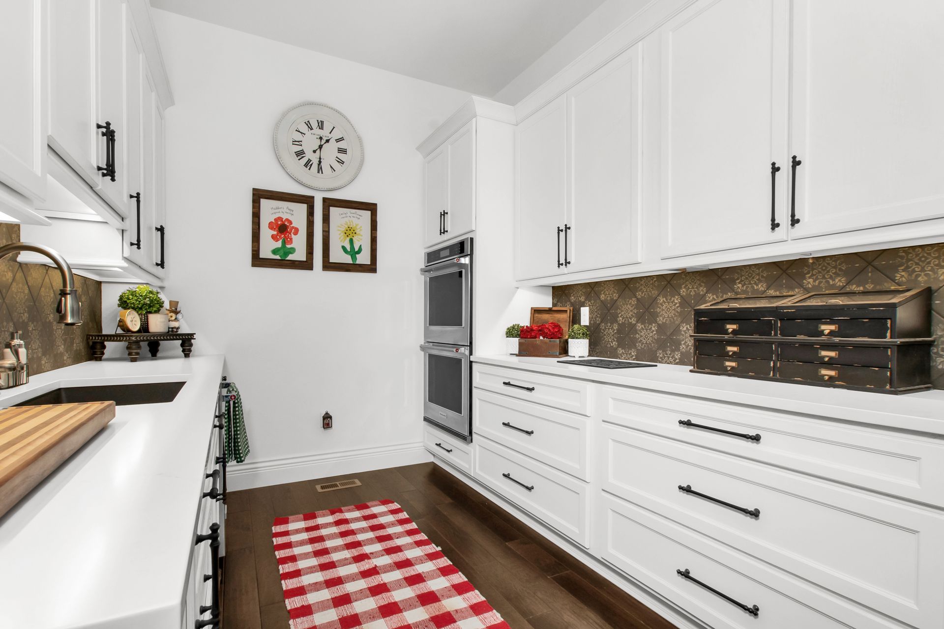 A kitchen with white cabinets and a red and white checkered rug.