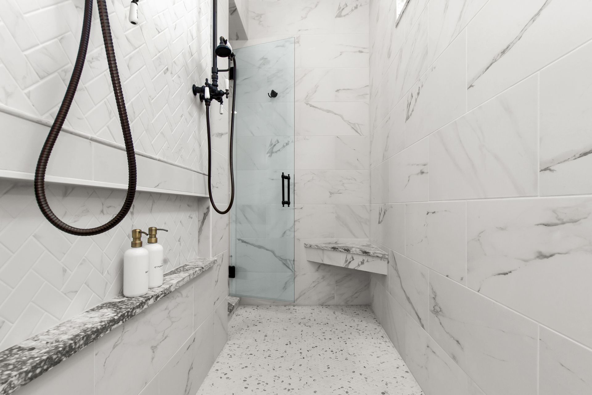 A bathroom with white tiles and a walk in shower with a glass door.