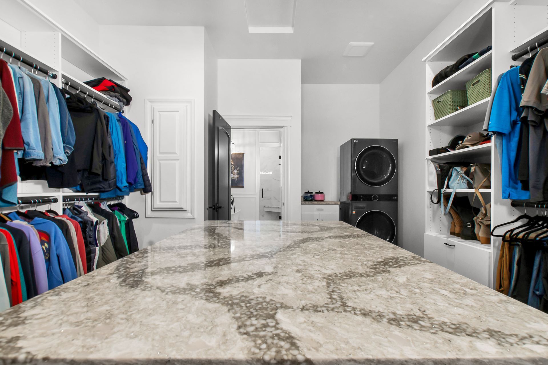 A large walk in closet with a marble counter top and clothes hanging on racks.
