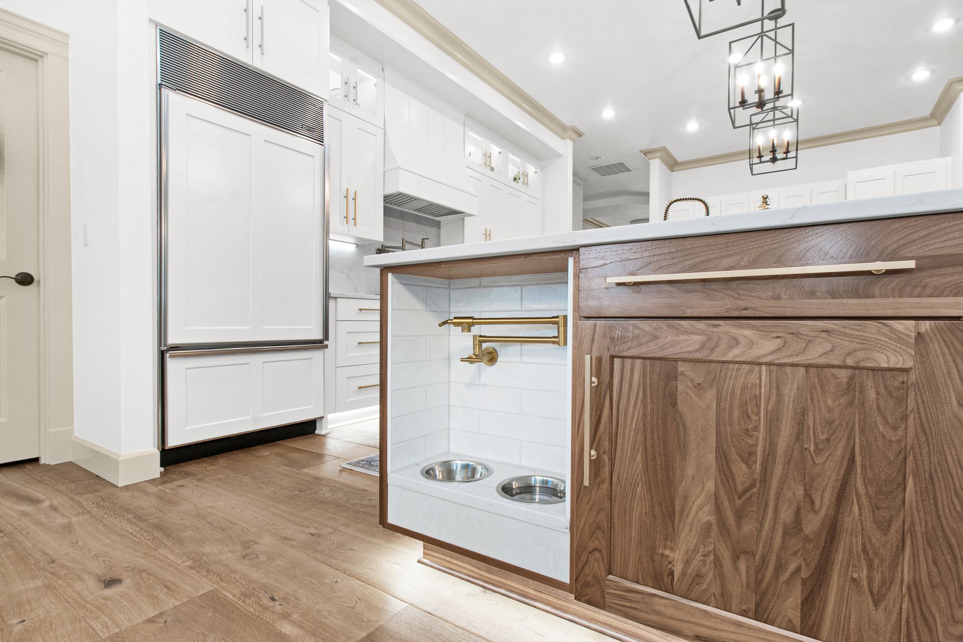 A kitchen with wooden cabinets , a refrigerator , and a dog bowl.