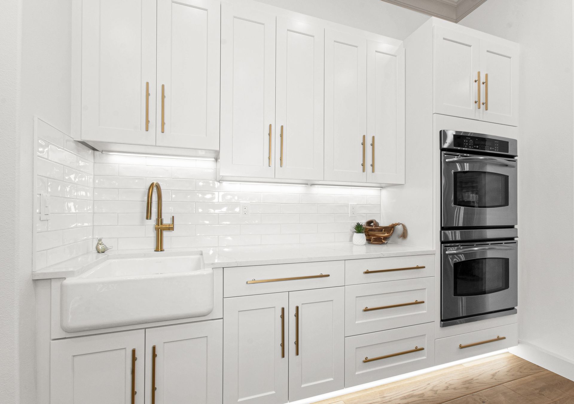 A kitchen with white cabinets , stainless steel appliances , a sink , and a double oven.
