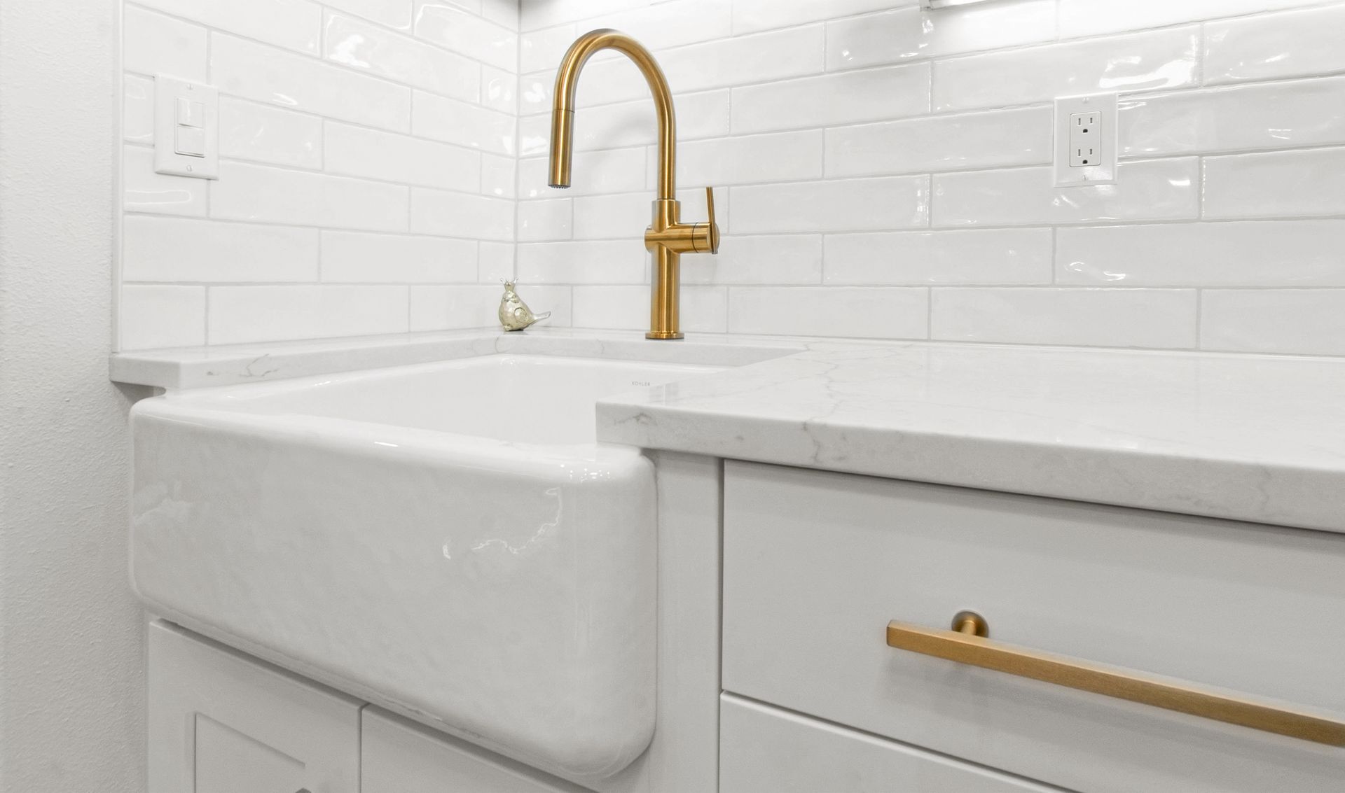 A kitchen sink with a gold faucet and white cabinets.