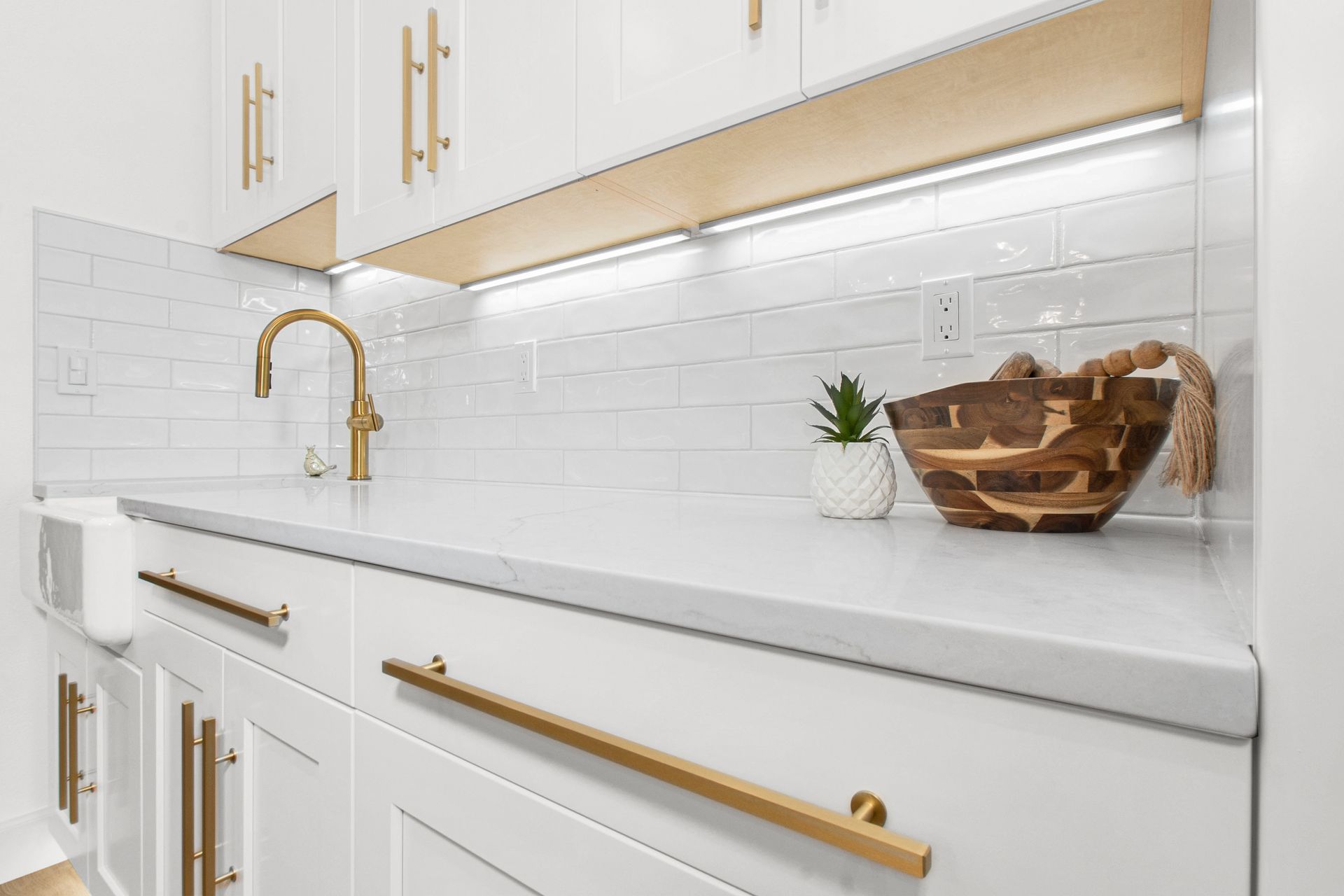 A kitchen with white cabinets and gold handles and a sink.