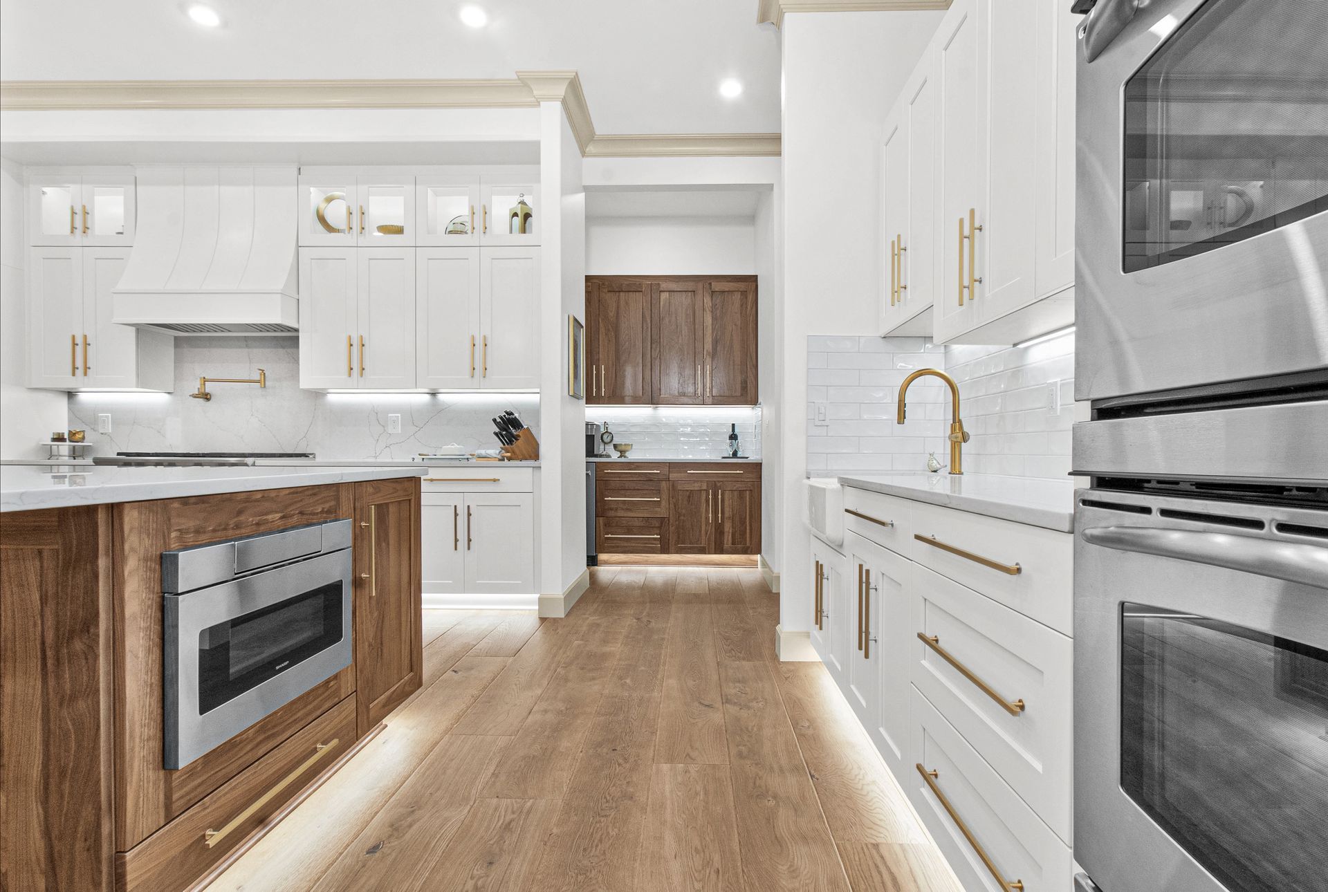 A kitchen with white cabinets and wooden floors and stainless steel appliances.