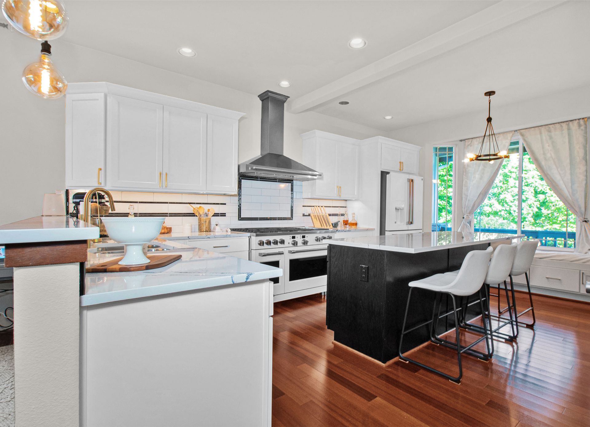 A kitchen with white cabinets , stainless steel appliances , hardwood floors and a large island.