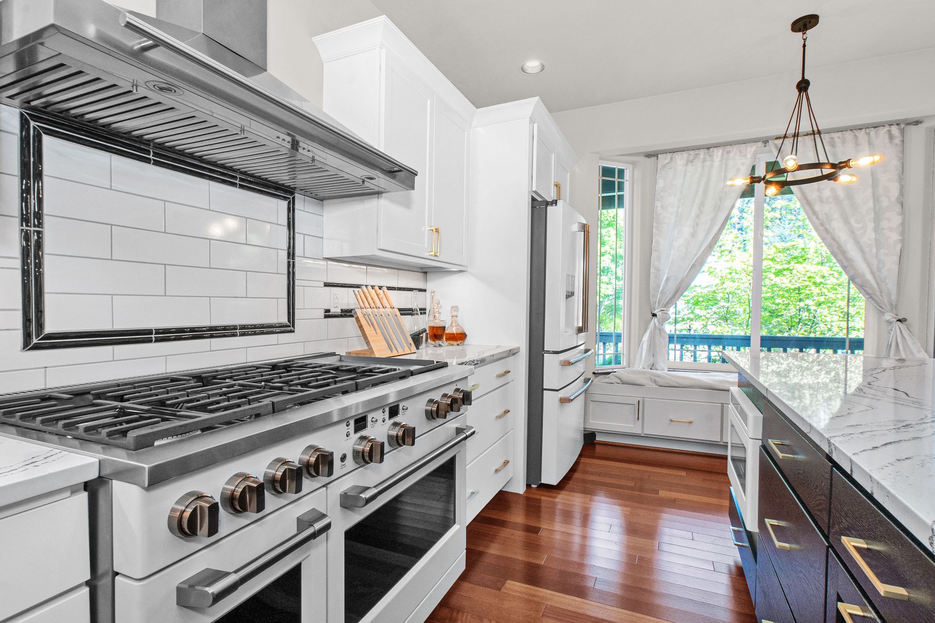 A kitchen with white cabinets , stainless steel appliances , hardwood floors and a large stove top oven.