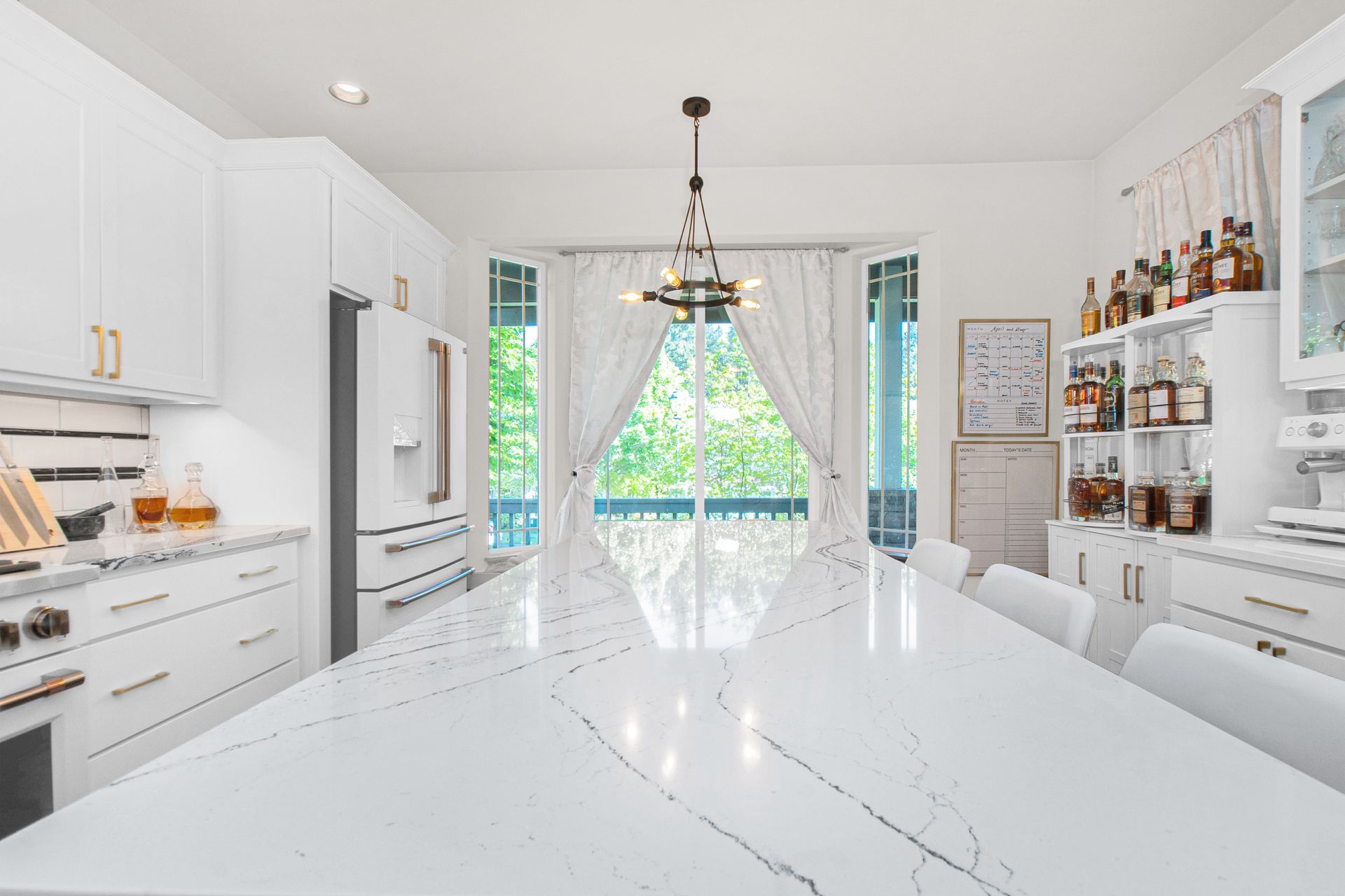 A kitchen with white cabinets , a large table , and a large window.