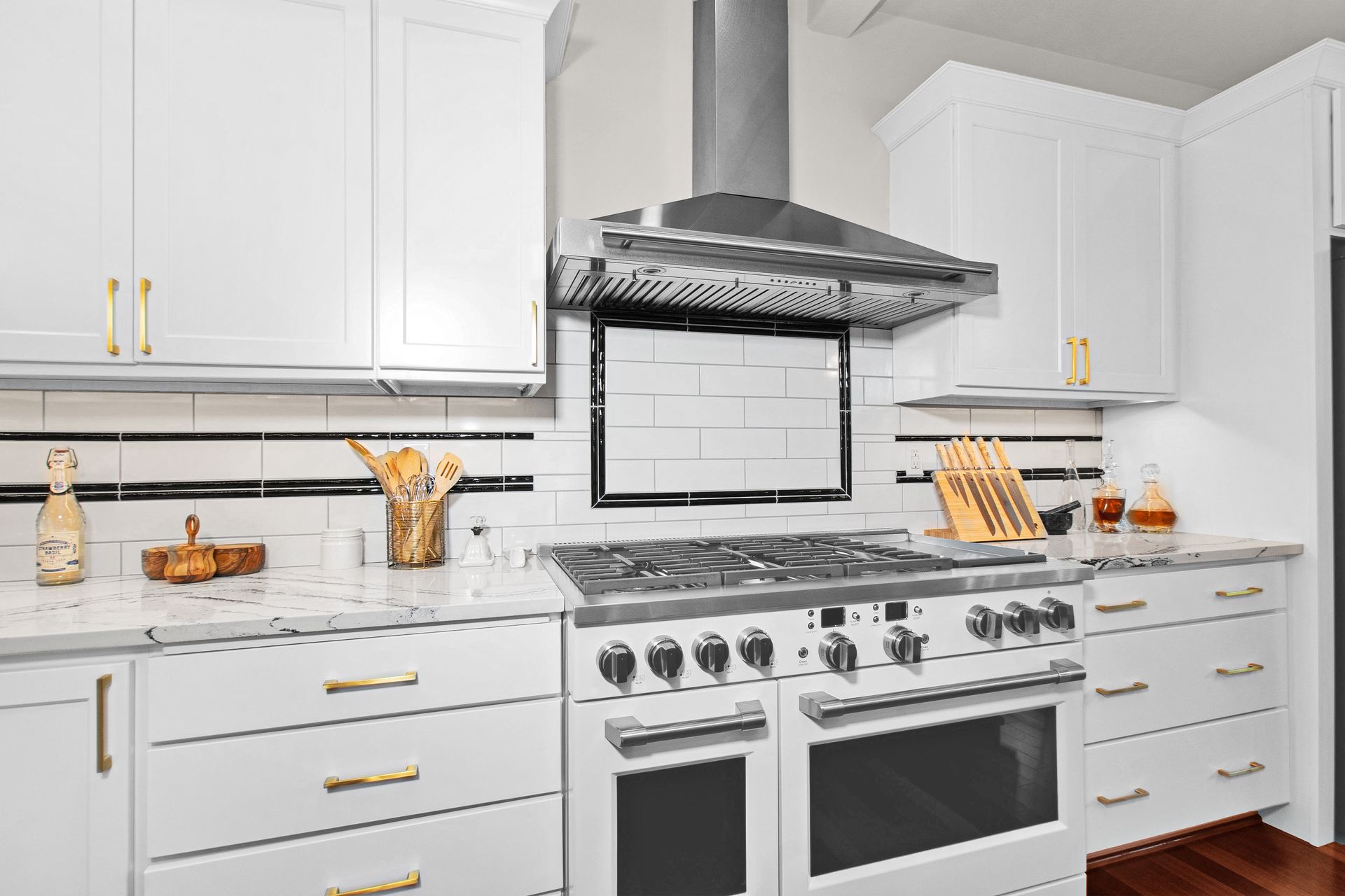A kitchen with white cabinets , a stove , and a hood.
