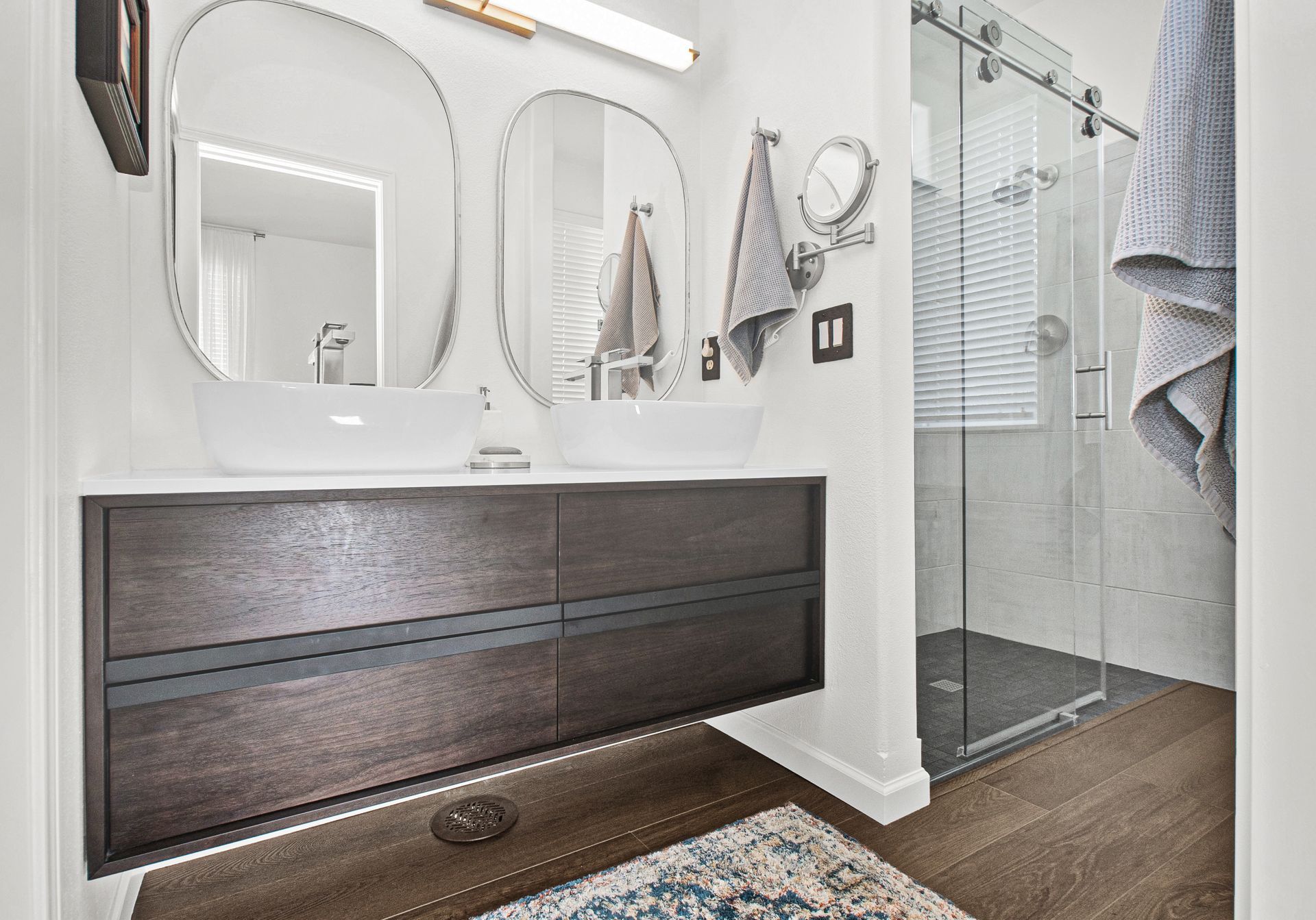 A bathroom with a sink , mirrors , and a walk in shower.