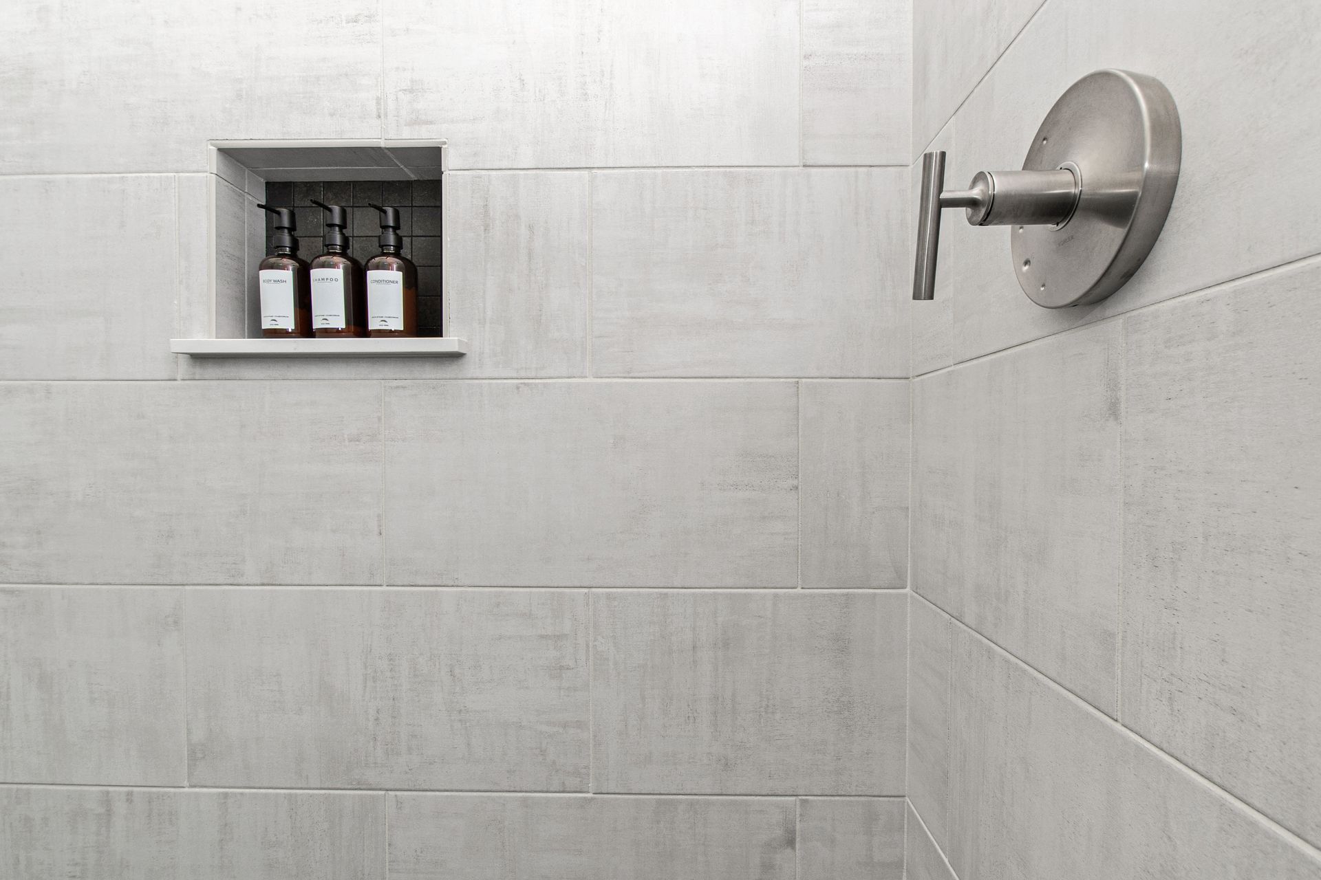 There are two bottles of soap on the shelf in the shower.