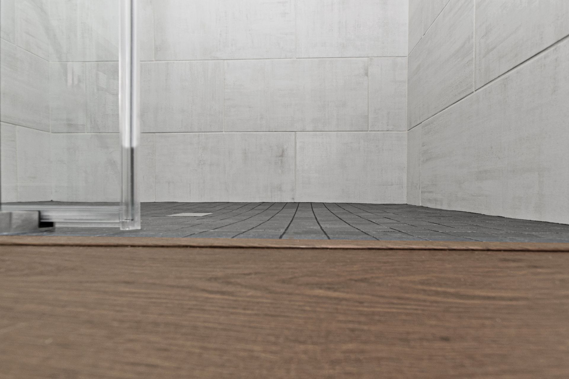 A shower with a wooden floor and a glass door.