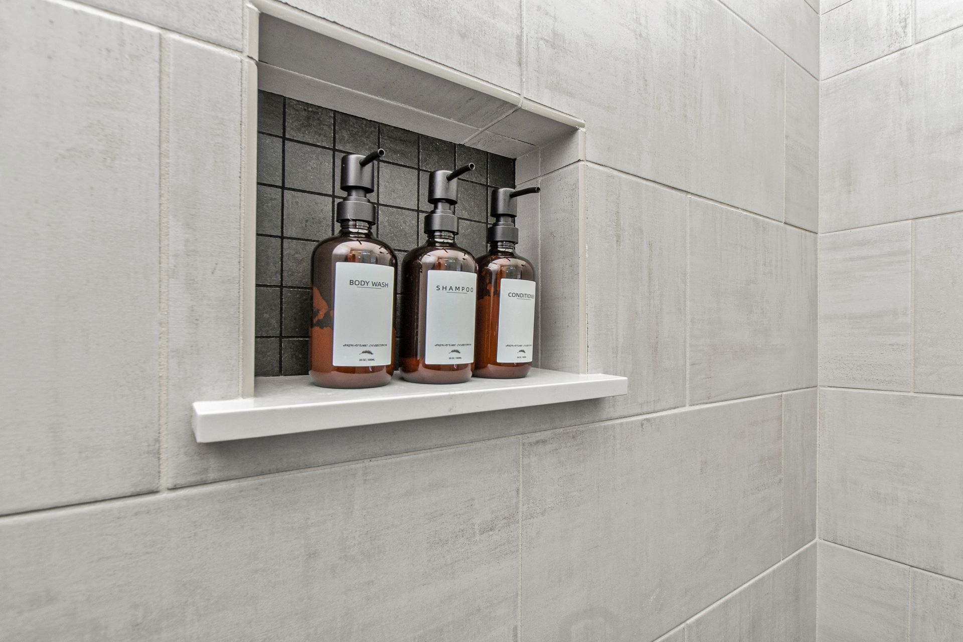Three bottles of soap are sitting on a shelf in a shower.