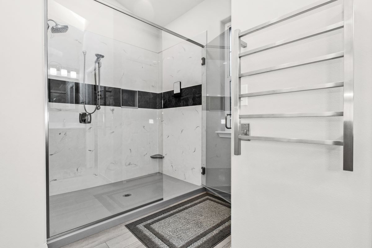 Bathroom with glass shower, tile floor, towel rack, and decorative rug.