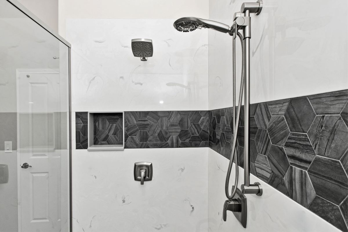 Bathroom with glass shower door, marble-like tiles, and black geometric accent. Showerhead and controls visible.
