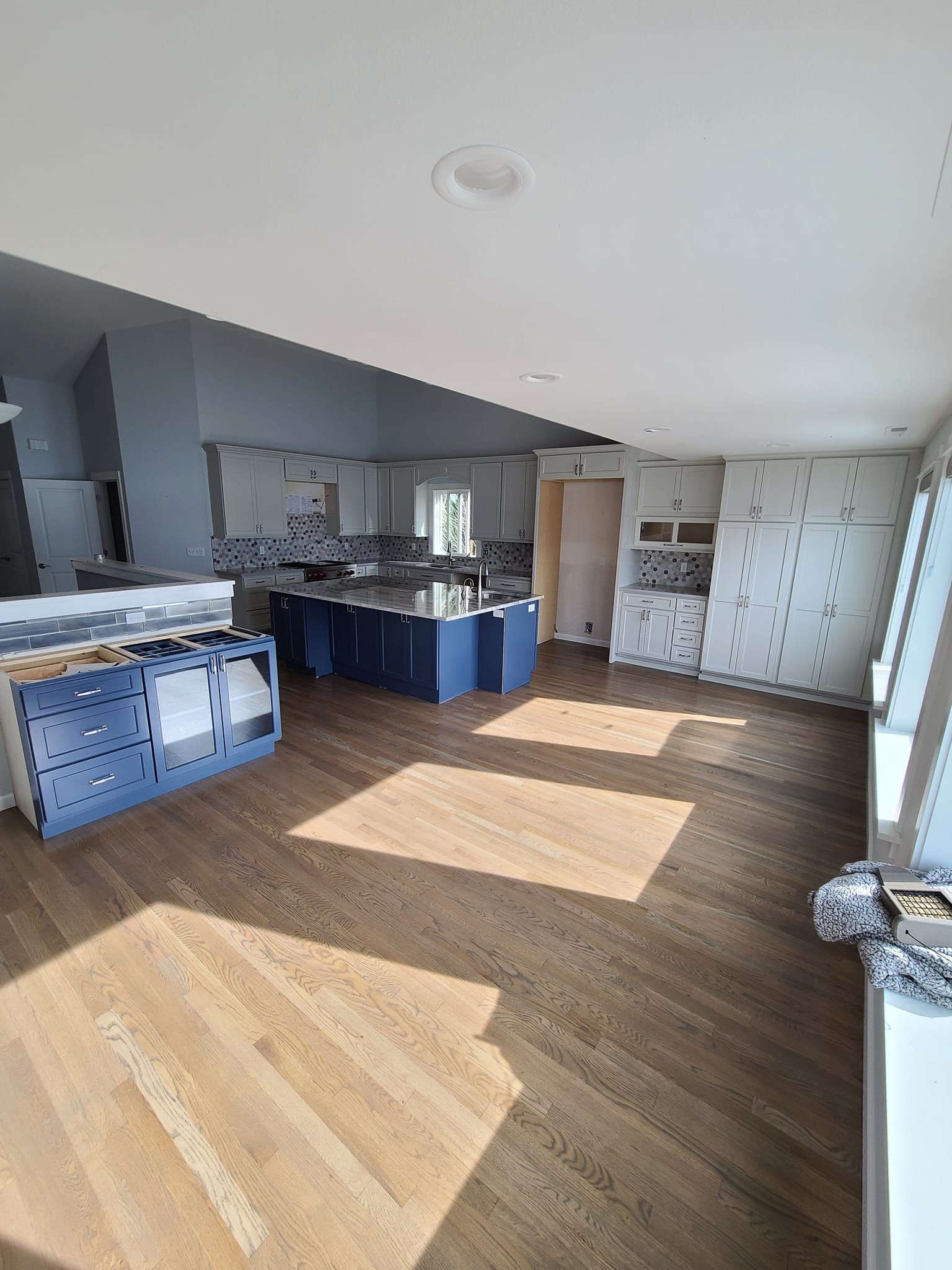 A kitchen with white cabinets , hardwood floors , stainless steel appliances and a rug on the floor.