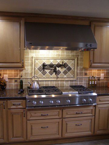 Stainless steel range and hood in a kitchen with tan cabinets and a tiled backsplash.