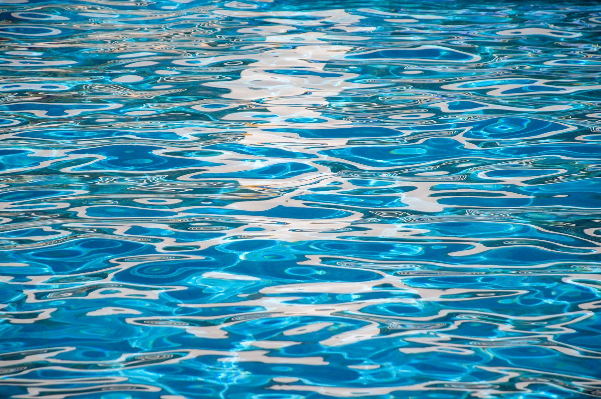Sunlit rippling blue swimming pool water surface with shimmering reflections on a clear day. Sunlit rippling blue swimming pool water surface with shimmering reflections on a clear day.
