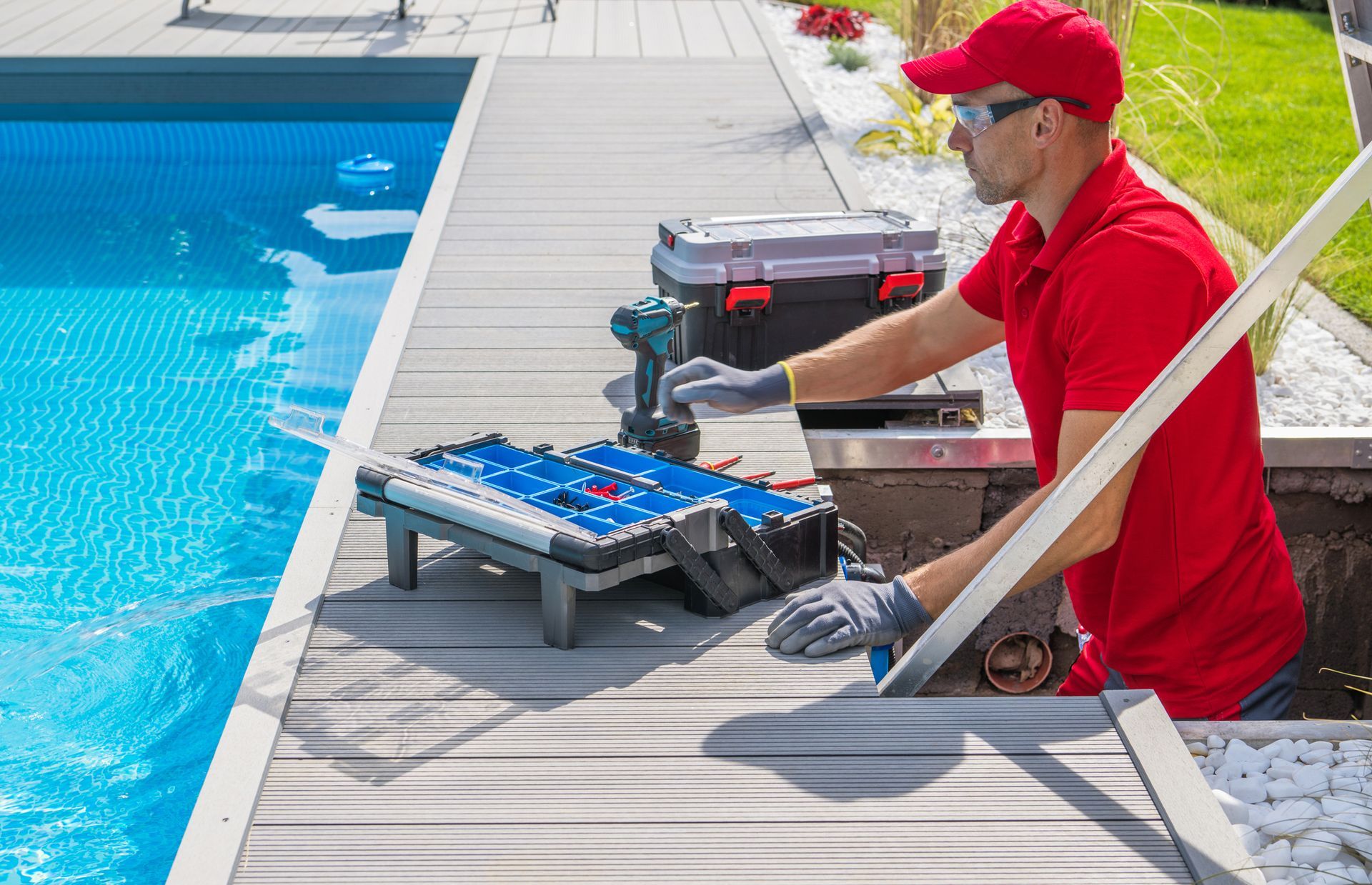 A technician in a red uniform with a toolbox in front of him, performs swimming pool maintenance.