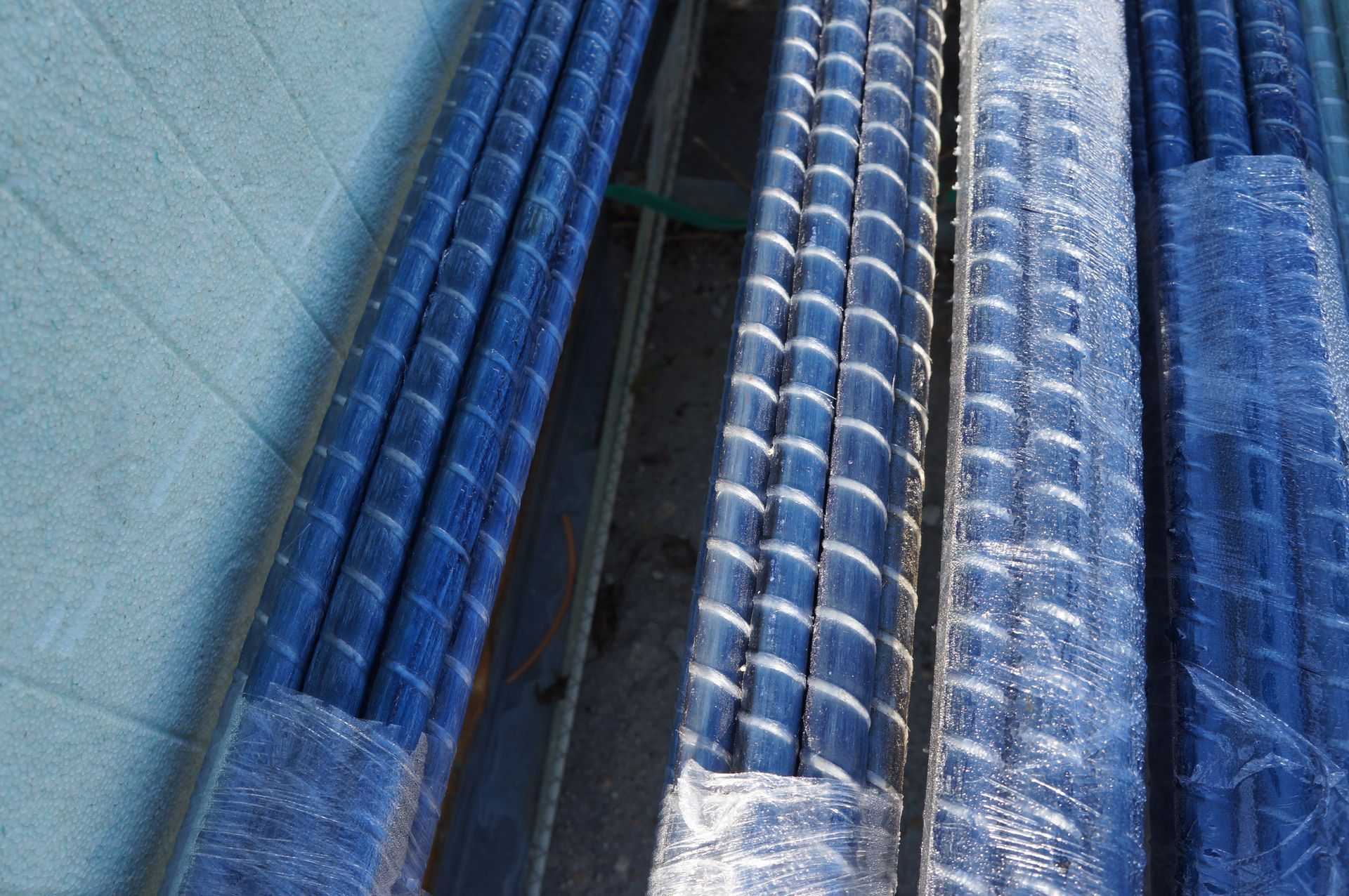 Bundled blue rebar, wrapped in plastic, stacked on a wooden frame, outdoors.