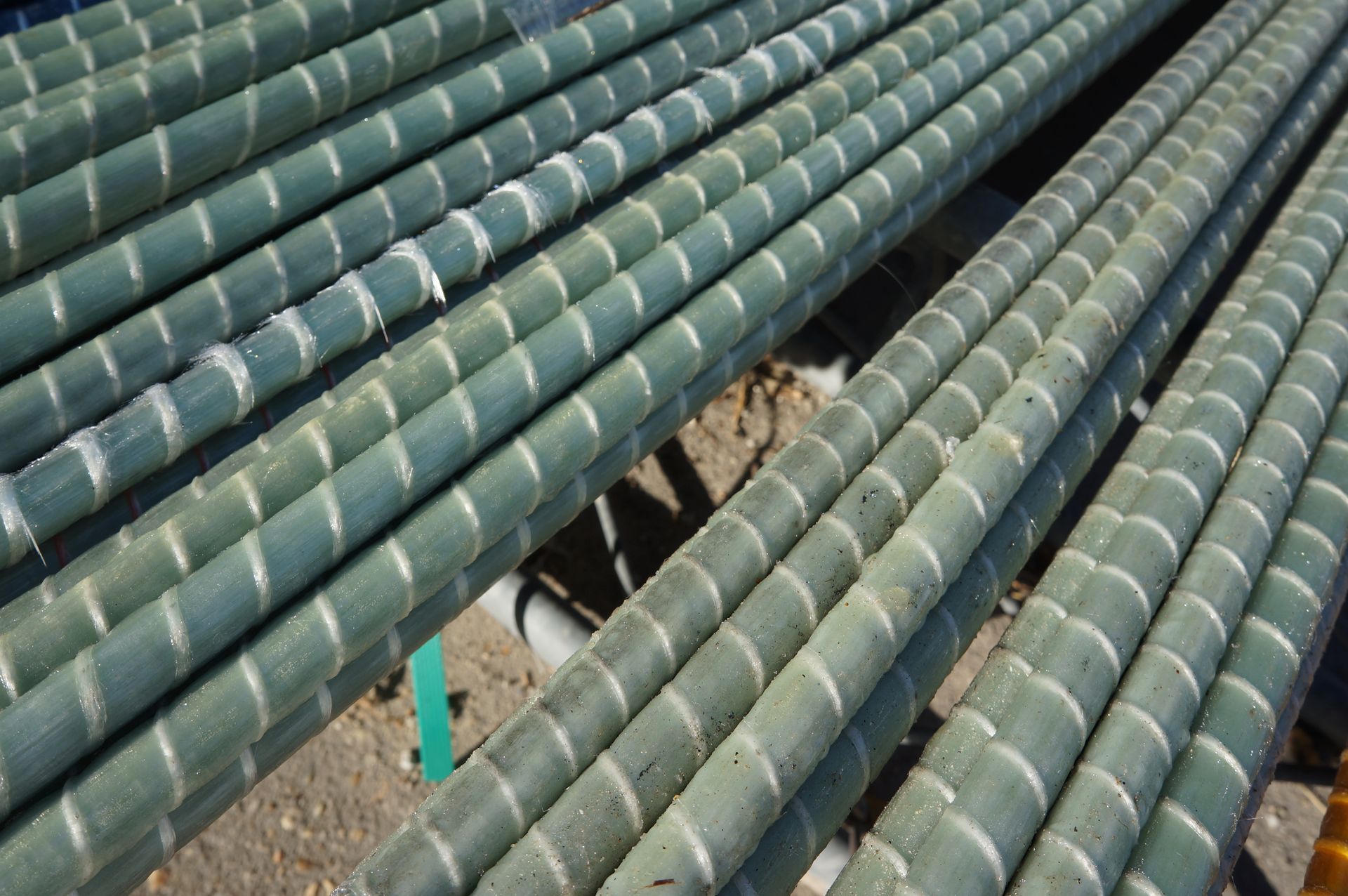 Green fiberglass rebar rods with spiral textures, stacked outdoors.