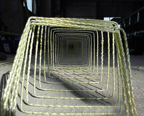 Square-shaped fiberglass reinforcement cage, viewed from the front, inside a construction setting.