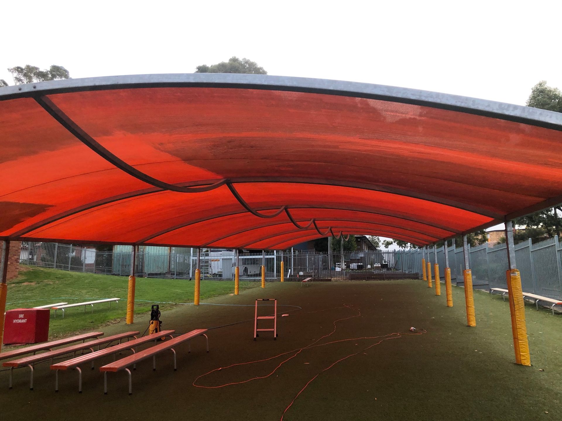 A row of benches under an orange canopy in a park.