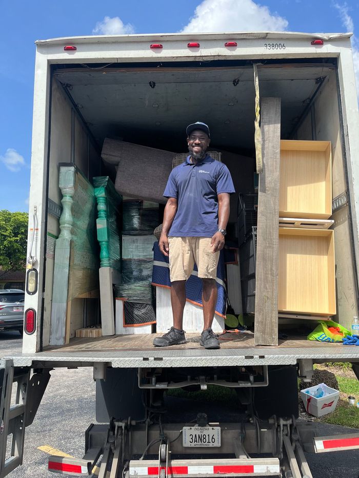 A man is standing on the back of a moving truck.