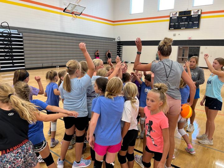 A group of young girls are standing in a gym with their hands in the air.