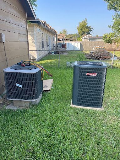 Two air conditioners are sitting in the grass in front of a house.