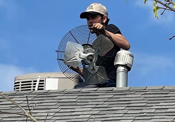 A man is sitting on top of a roof holding a fan.