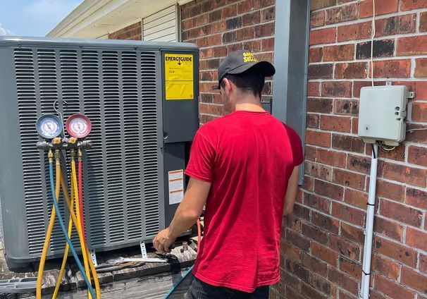 A man in a red shirt is working on an air conditioner outside of a brick building.