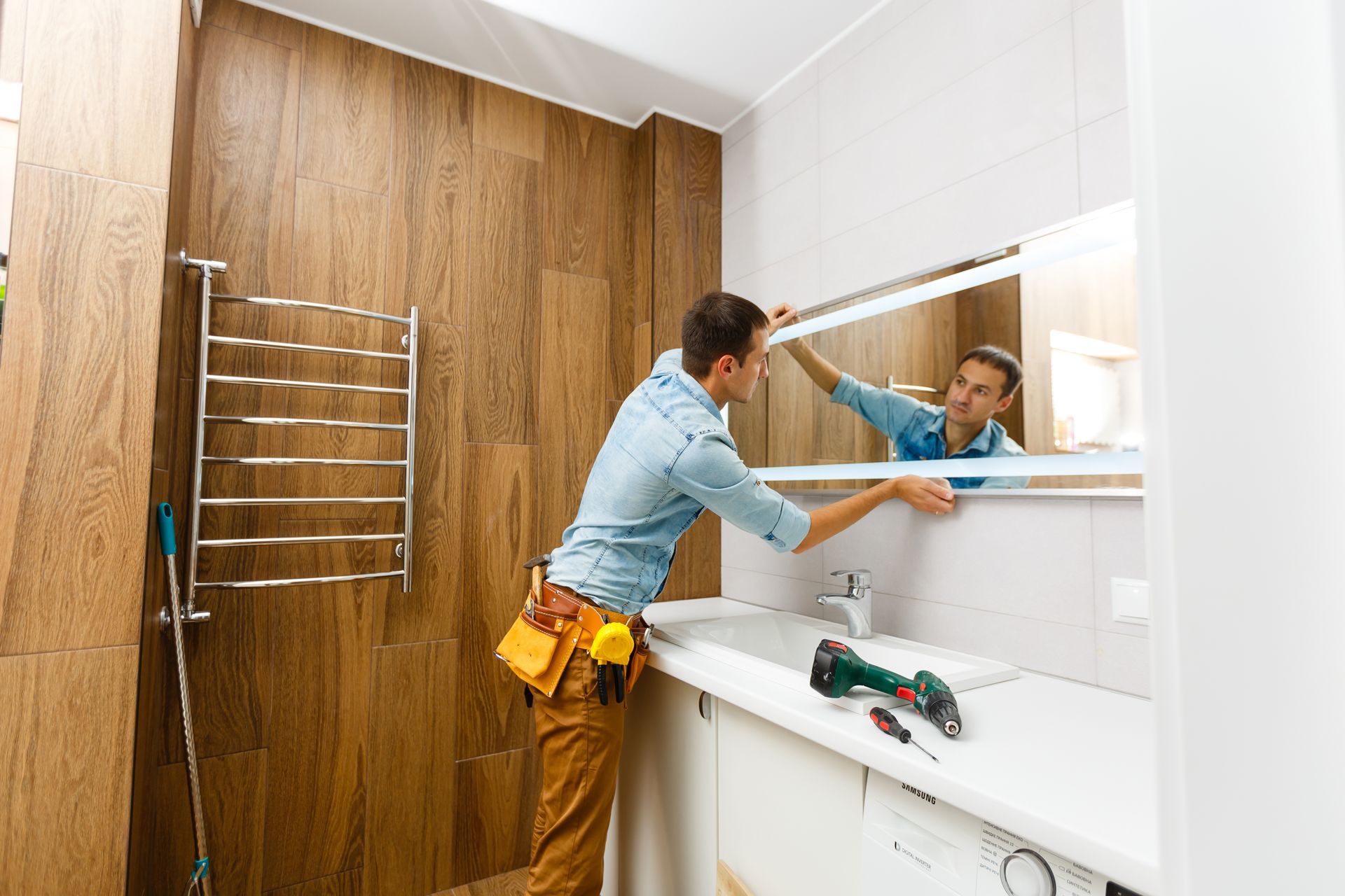Man installing a mirror on wall in his renewed bathroom
